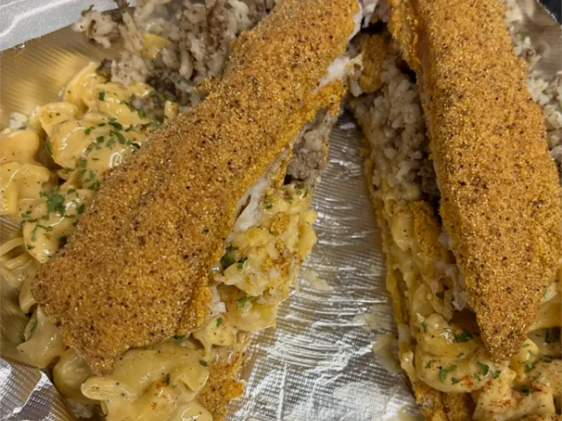 Two cornmeal-crusted catfish fillets stuffed with mac and cheese and dirty rice, on foil in a takeout box