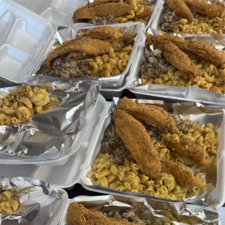 Rows of open takeout boxes, each with crusted catfish fillets over mac and cheese and dirty rice